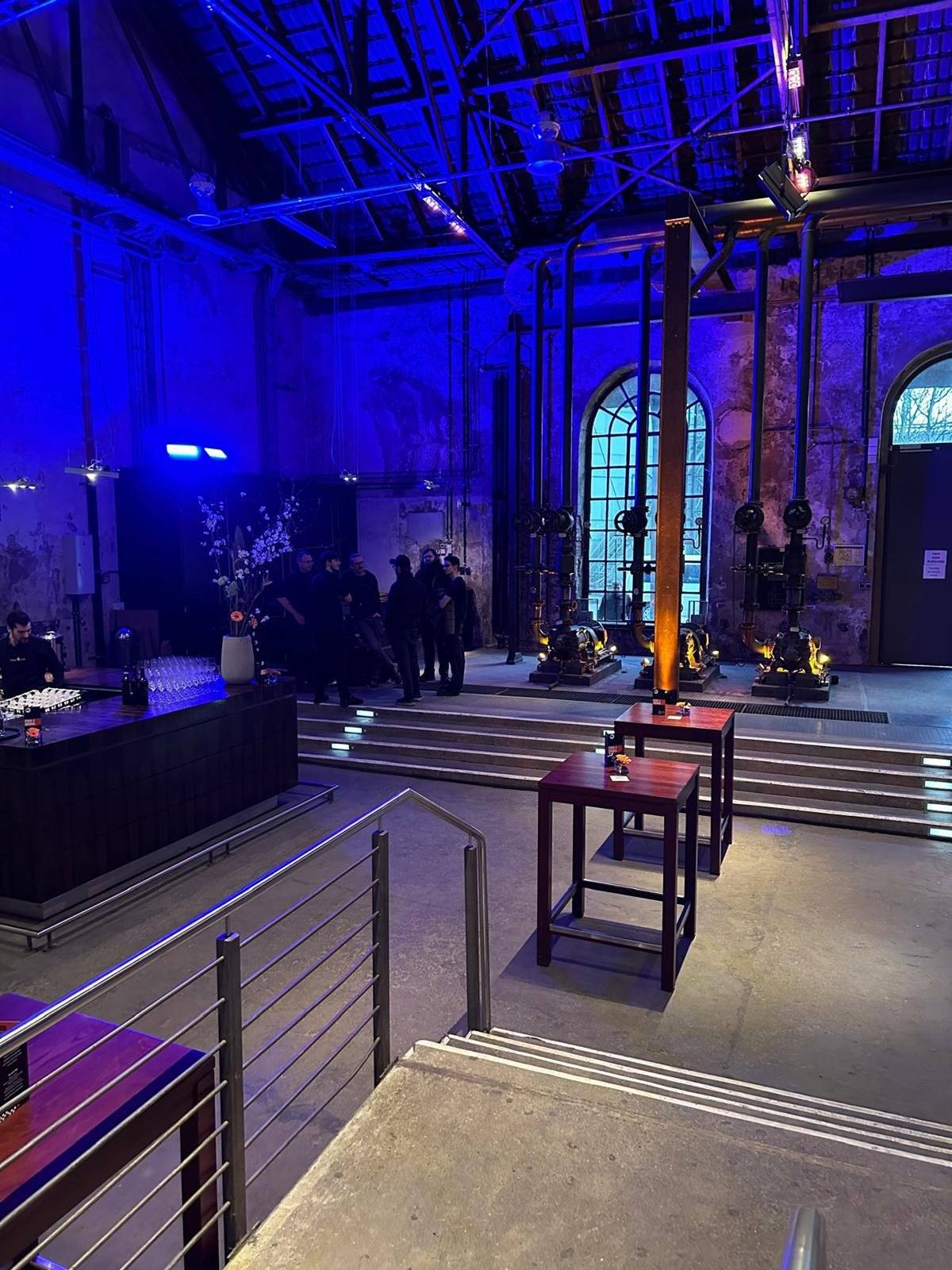 Blau beleuchtete Eventlocation in einer Industriehalle mit Bar und Stehtischen
